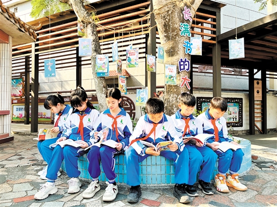 龙口镇协华小学学生围坐在“长满书的大树”下捧书共读，成为该校一道亮丽的风景线。