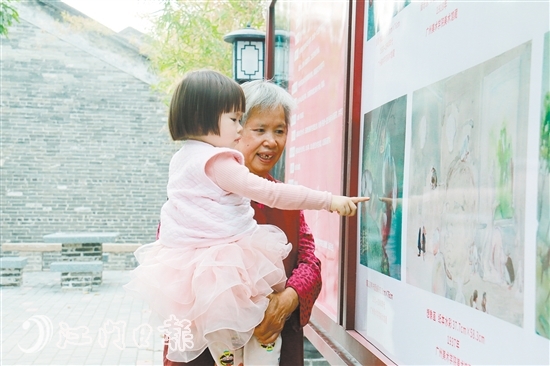 陈山村一位小朋友与奶奶一起看油画作品图片。
