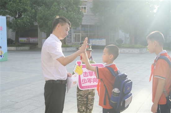 紫茶小学党委书记谭国池与学生逐一击掌。