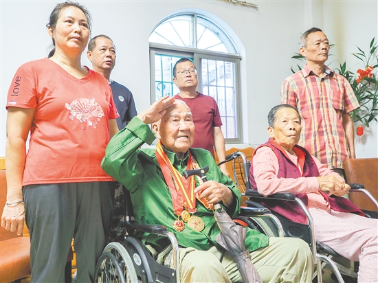 在鹤山市鹤城镇的家中，抗战老战士黄光华一边观看阅兵仪式直播，一边用右手敬礼。