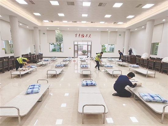 工作人员正在临时庇护场所铺设床位。 工作人员正在临时庇护场所铺设床位。