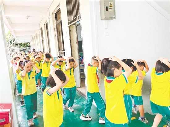 演练中，学生双手抱头、紧贴墙角，按照指定的逃生路线快速有序地撤离至操场安全区域。