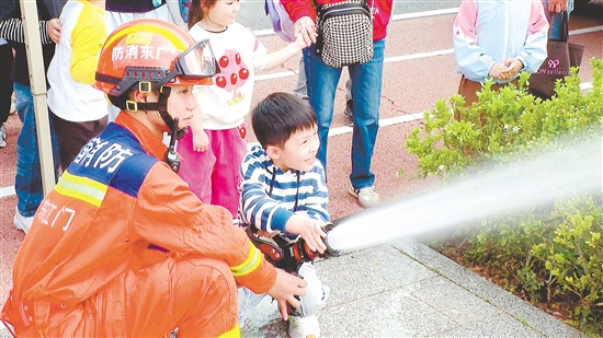 在消防员的指导下，小朋友体验使用消防水枪。