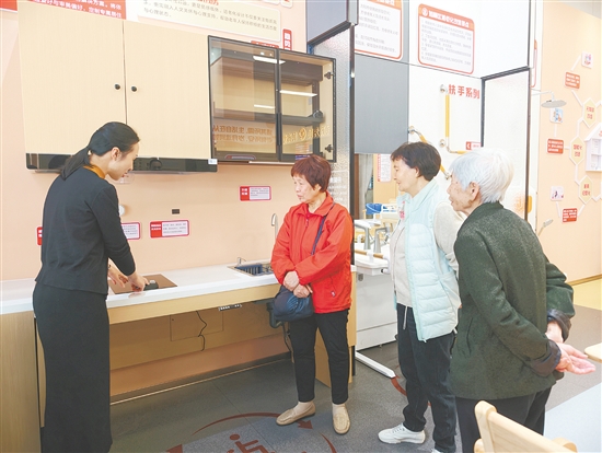 工作人员（左一）向长者介绍适老化厨房燃气灶，其具有防干烧和自动熄火功能。